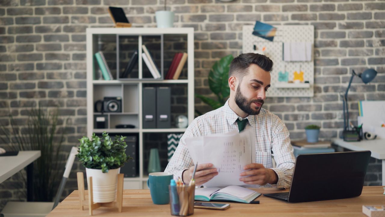 about-us Young professional man at desk with laptop and documents in a modern office.