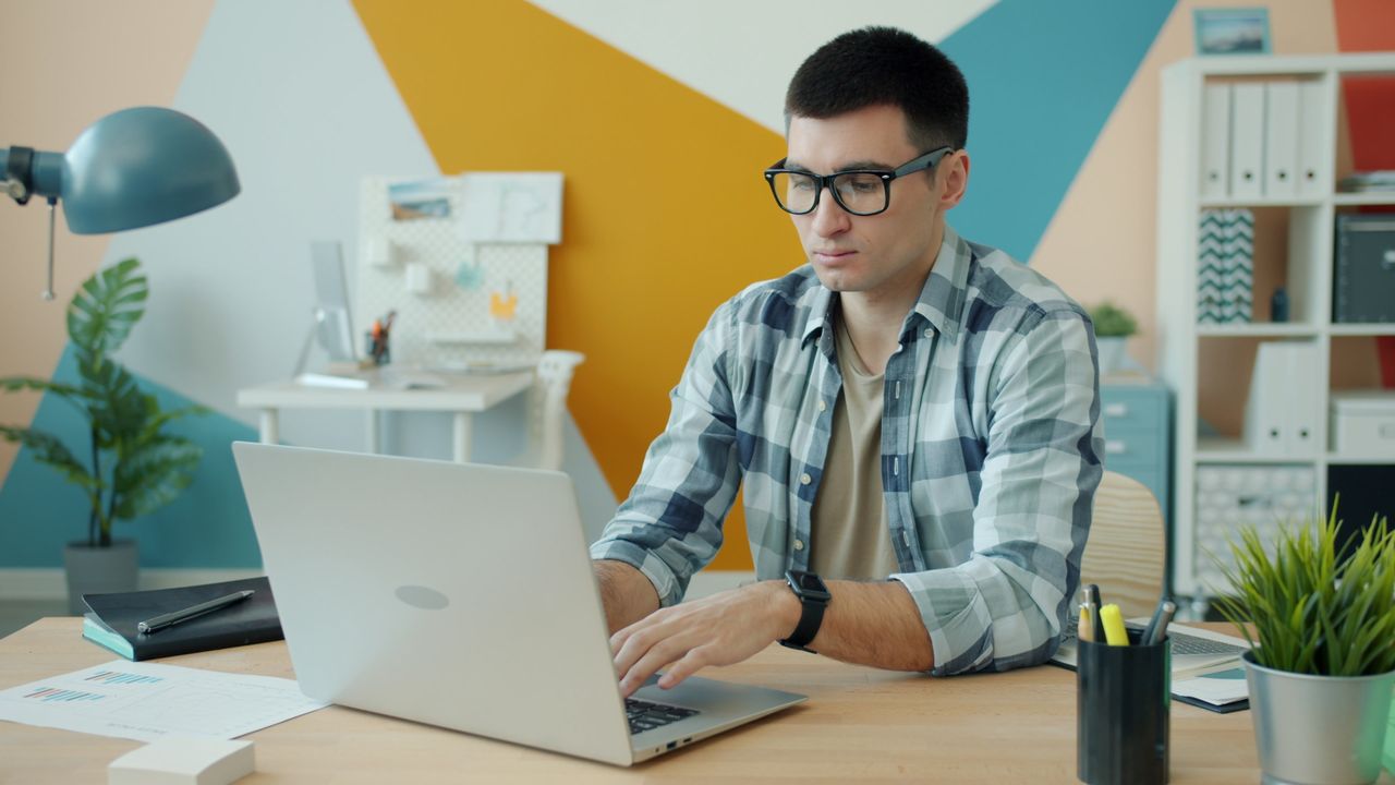 about-us Focused young man wearing glasses, working on a laptop in a stylish office.