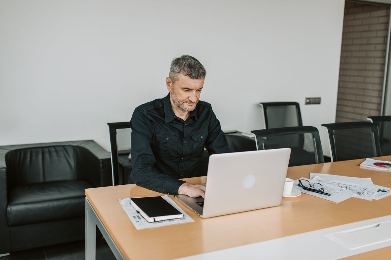 Mature man focusing on his laptop while working in a modern office environment.