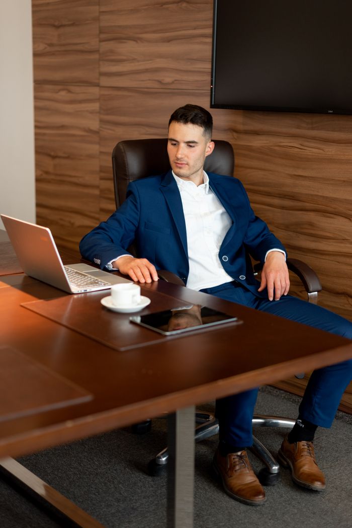 Confident young businessman in a suit working on a laptop at a wooden desk.