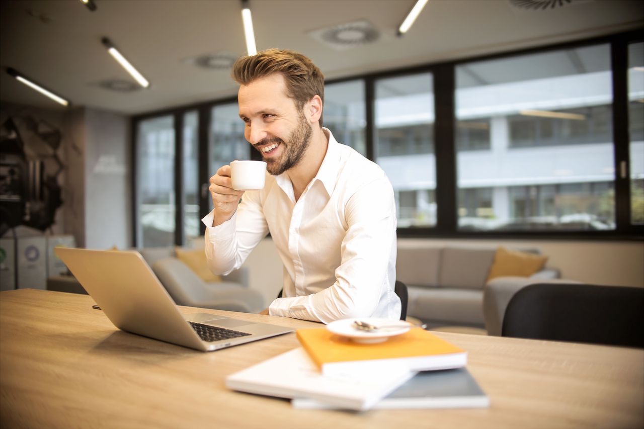 who-we-are Man enjoying a coffee break while working in a modern office with laptop and books.